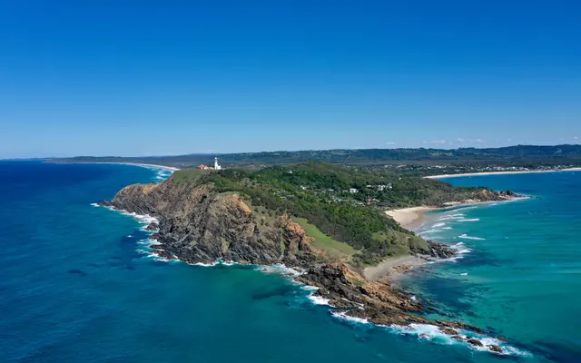 Cape Byron and its lighthouse from the air, with the beaches of Byron Bay behind
