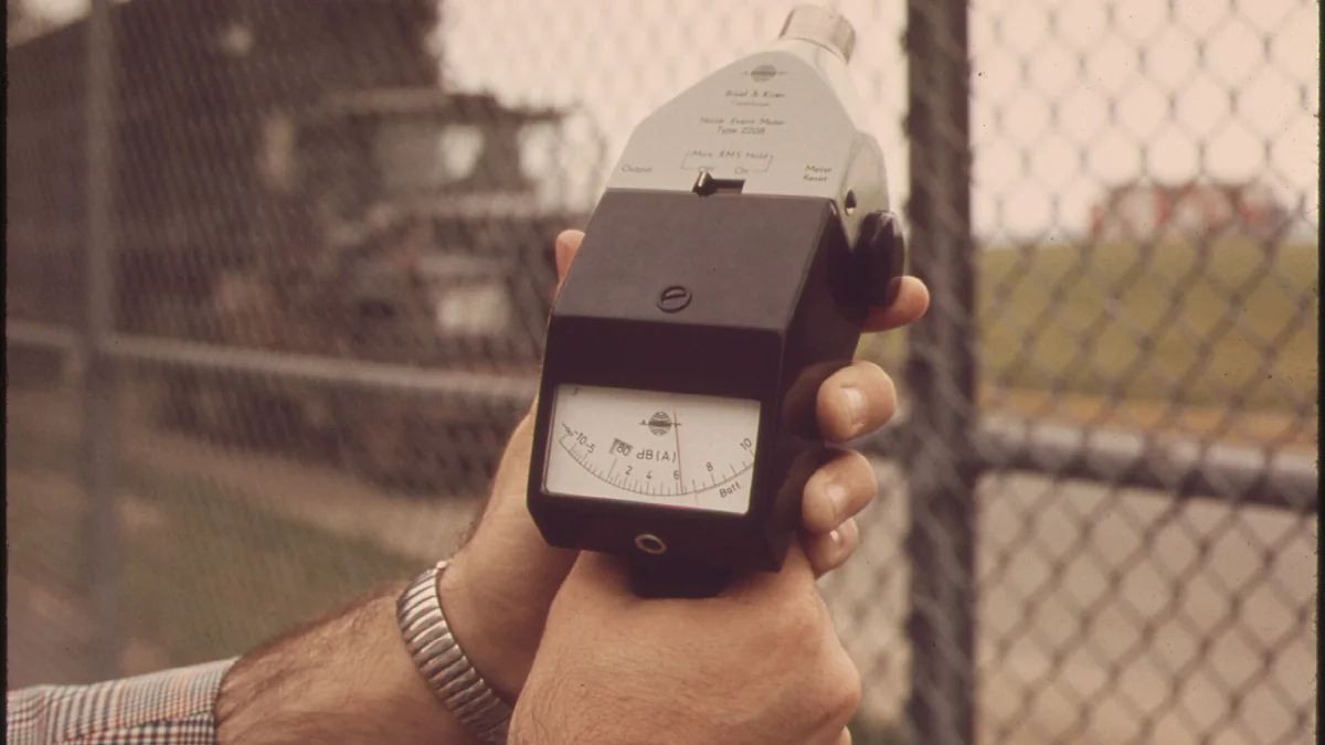 A hand holding a sound level meter beside an airport fence