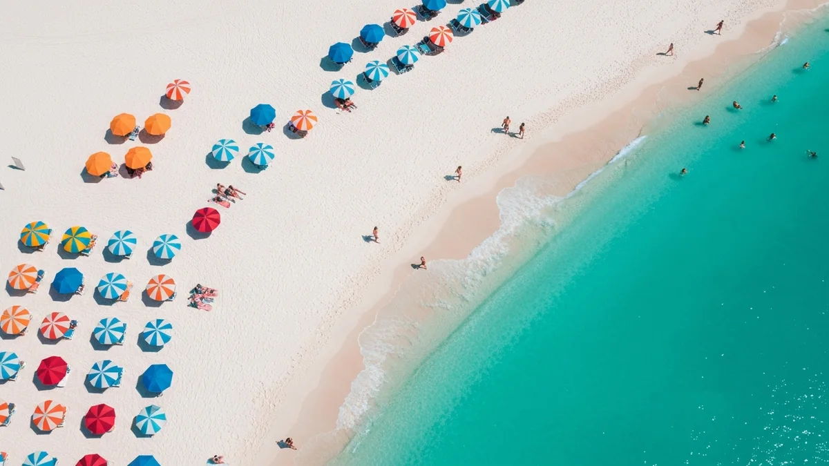 An overhead view of colorful beach umbrellas on sugar-white sand beside turquoise Gulf water