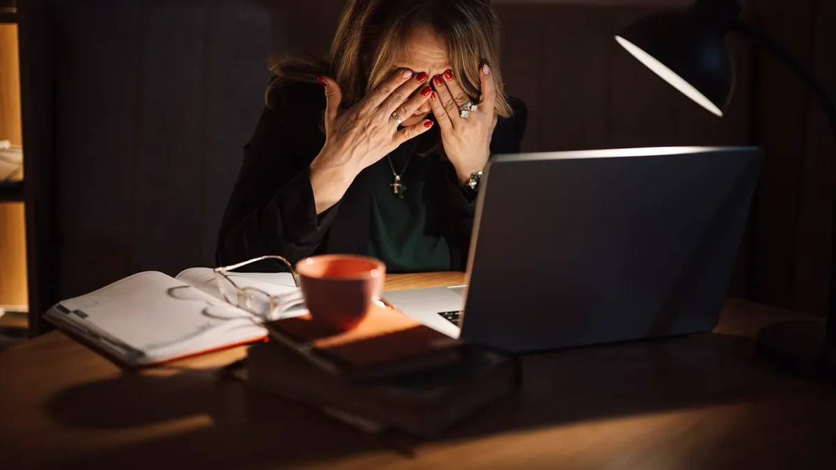 A woman at a laptop late at night with her head in her hands