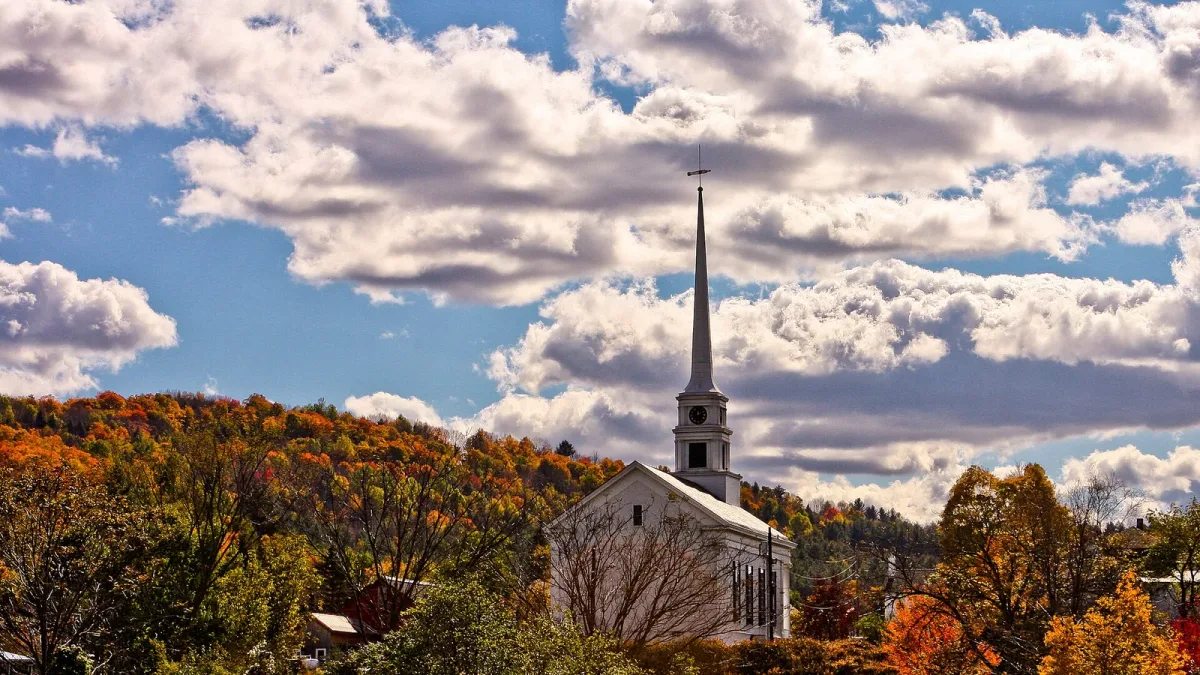 White-steepled New England village church surrounded by brilliant red and orange fall foliage in Stowe, Vermont