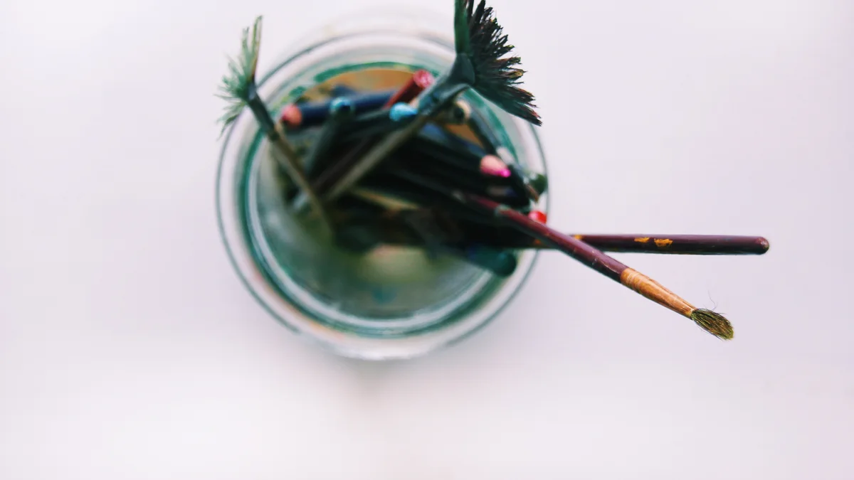 A glass jar holding a collection of used paint brushes