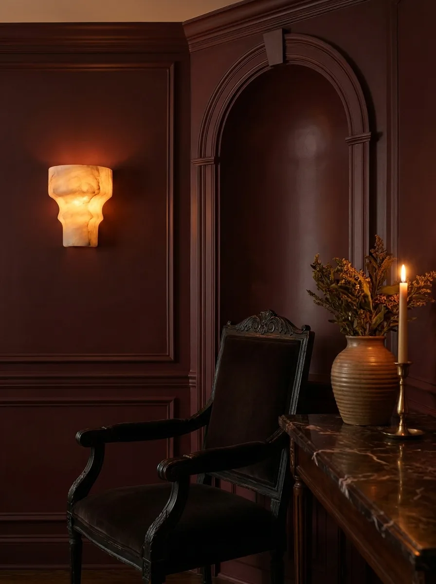 A color-drenched oxblood dining corner with a carved vintage chair, an alabaster wall sconce and a marble console