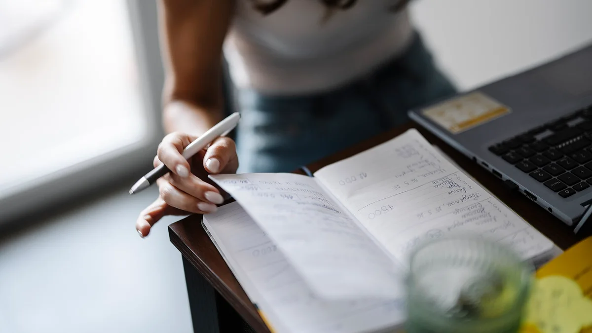 A person writing in a notebook while sitting at a desk