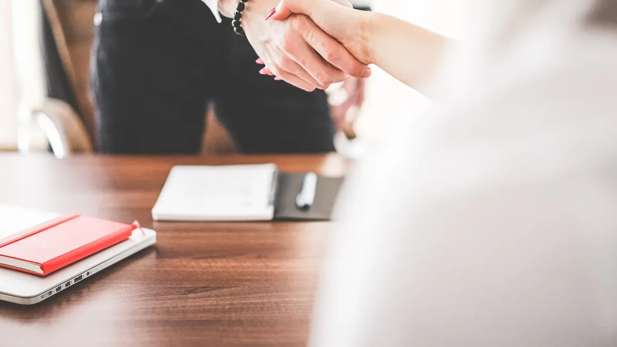 A businessman and businesswoman shaking hands across an office desk