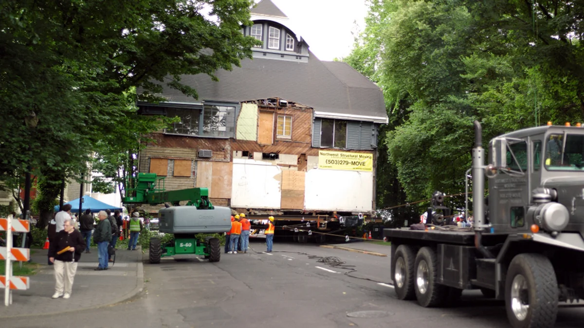 A large historic house being moved down a city street on a truck