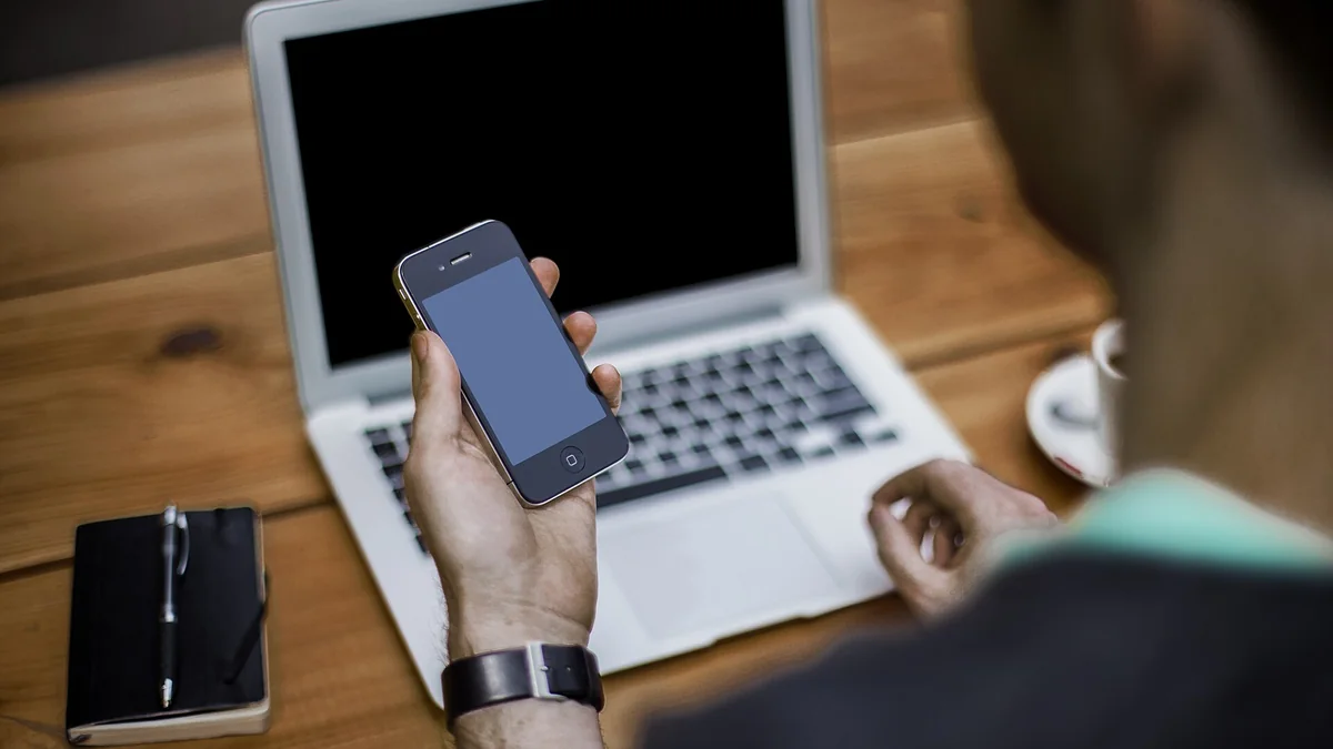 A person holding a smartphone in front of a laptop