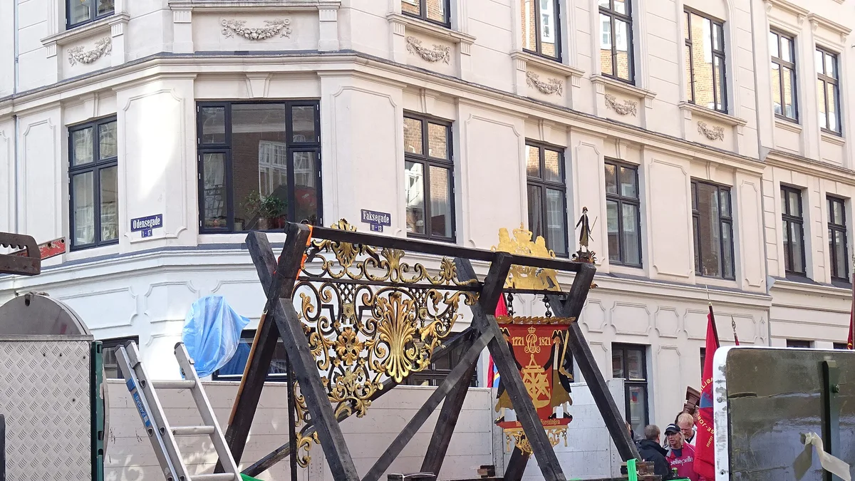 Craftsmen hanging a handmade wrought-iron shop sign above a doorway