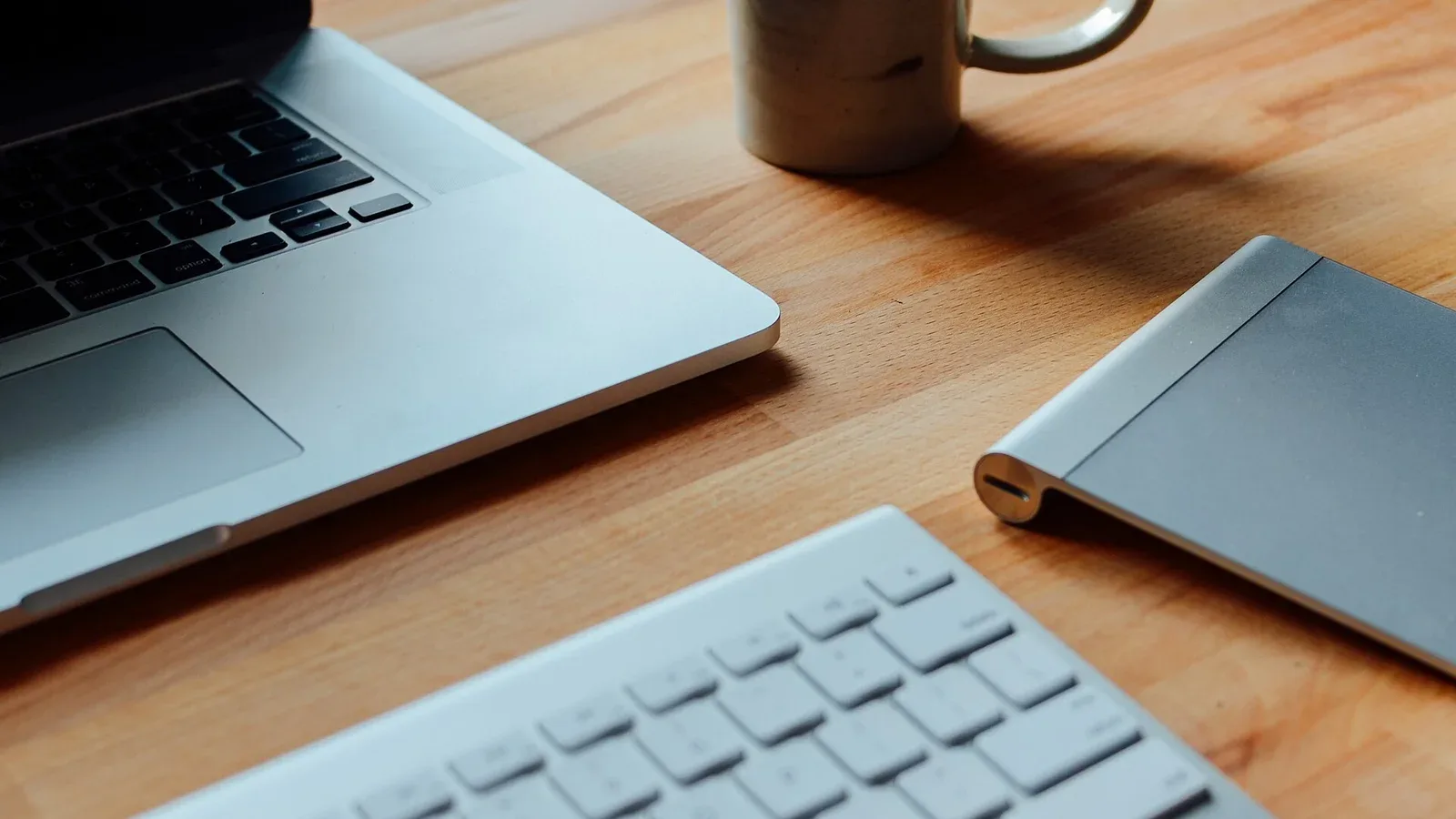 A laptop, keyboard and mug on a wooden desk
