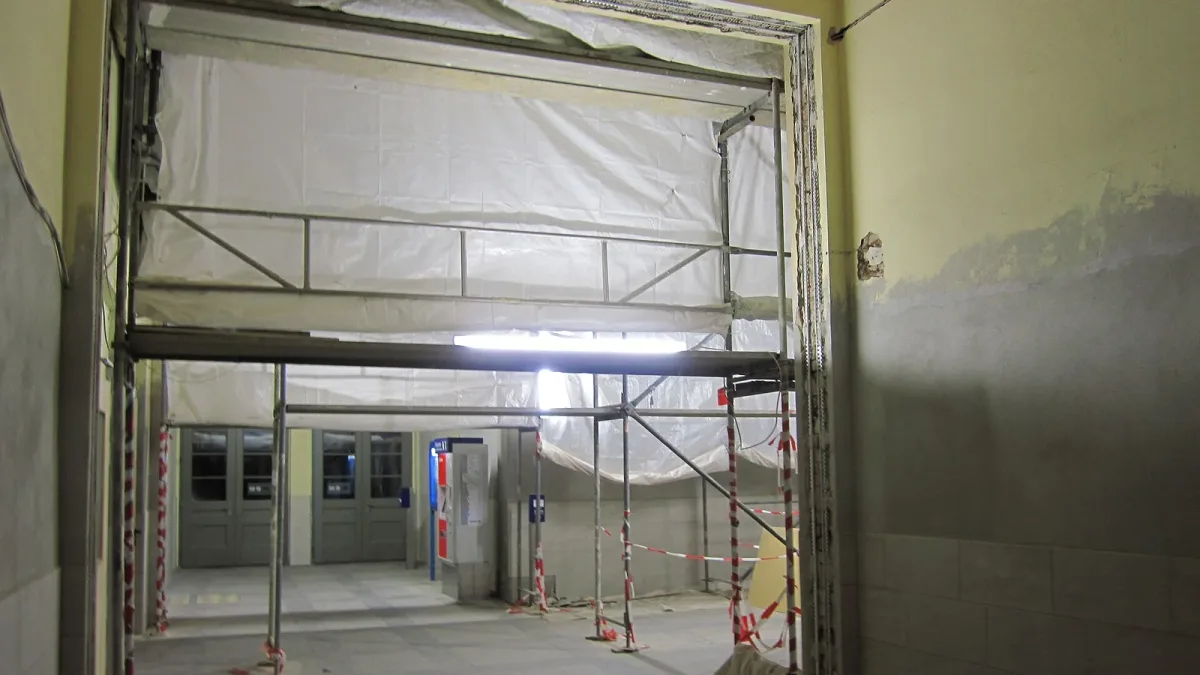 A building interior stripped back for renovation, with scaffolding and plastic sheeting