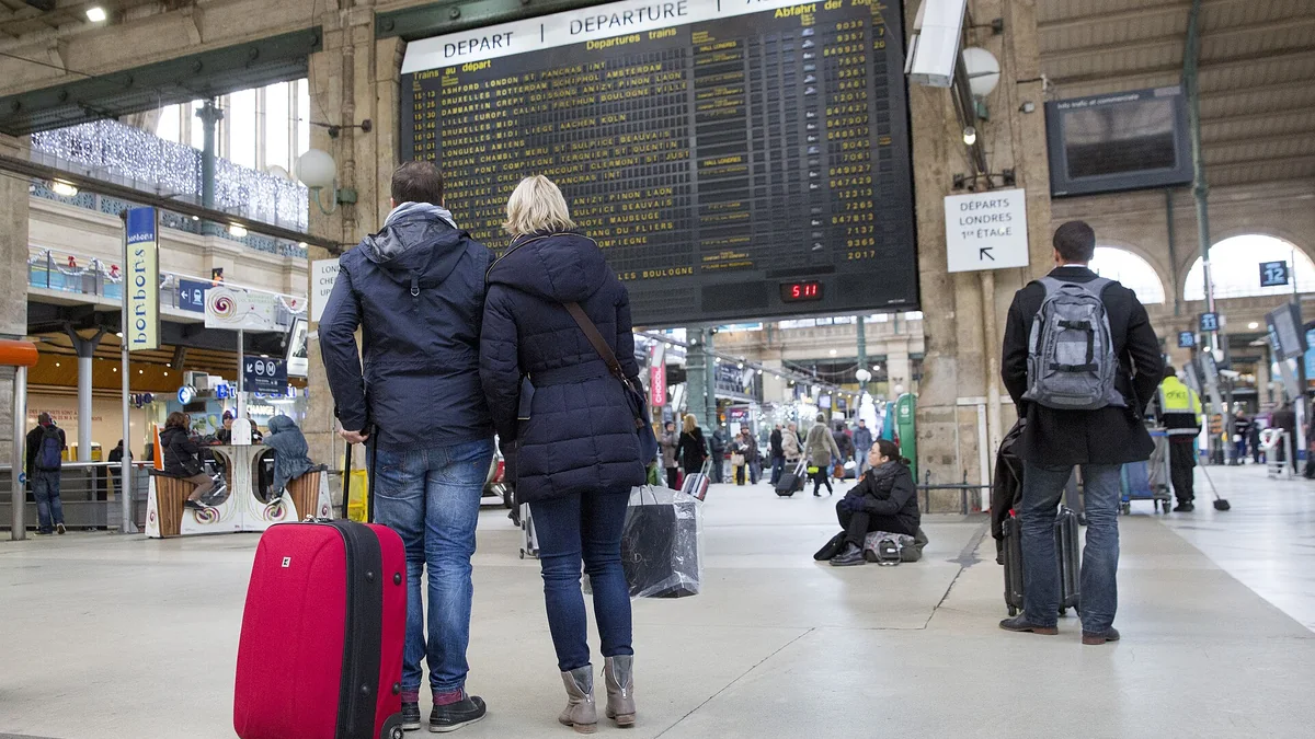 Travelers with suitcases reading the departures board in a train station