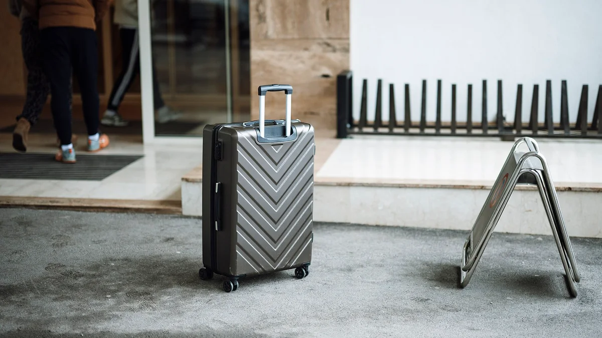 Travelers with luggage arriving at an entrance while a suitcase waits on the pavement