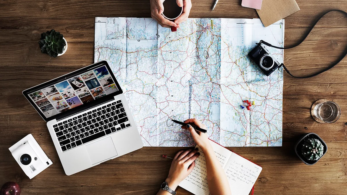 A laptop and a map spread across a table with coffee, mid trip-planning session
