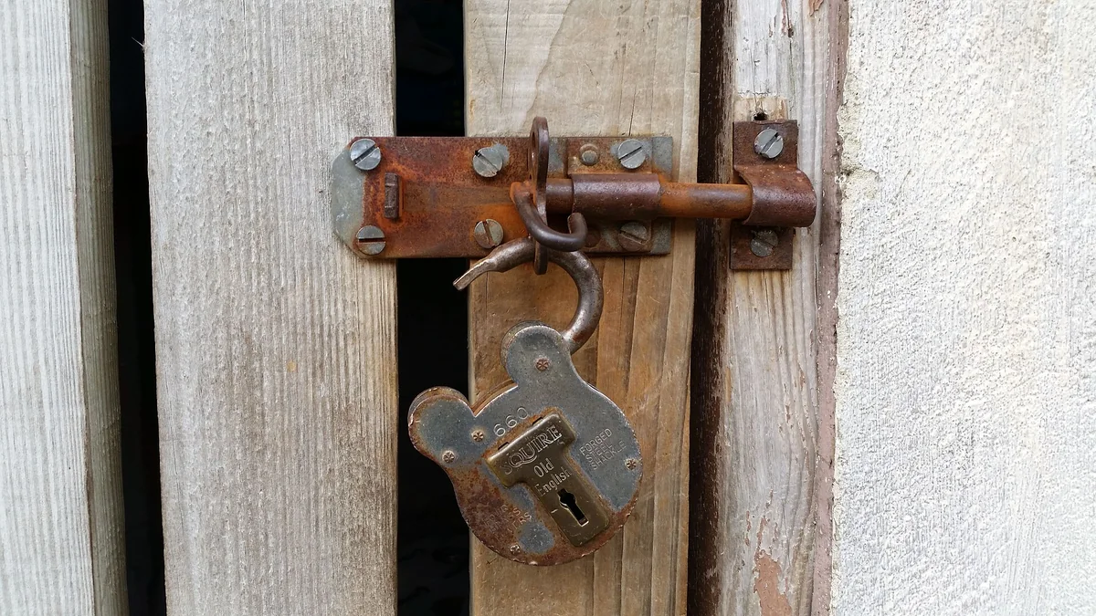 A rusted padlock and latch on an old wooden door