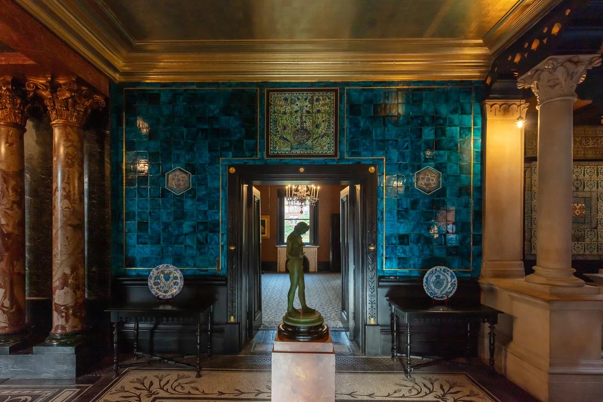 A hall lined with peacock blue glazed tiles, marble columns, a mosaic floor and a bronze statue