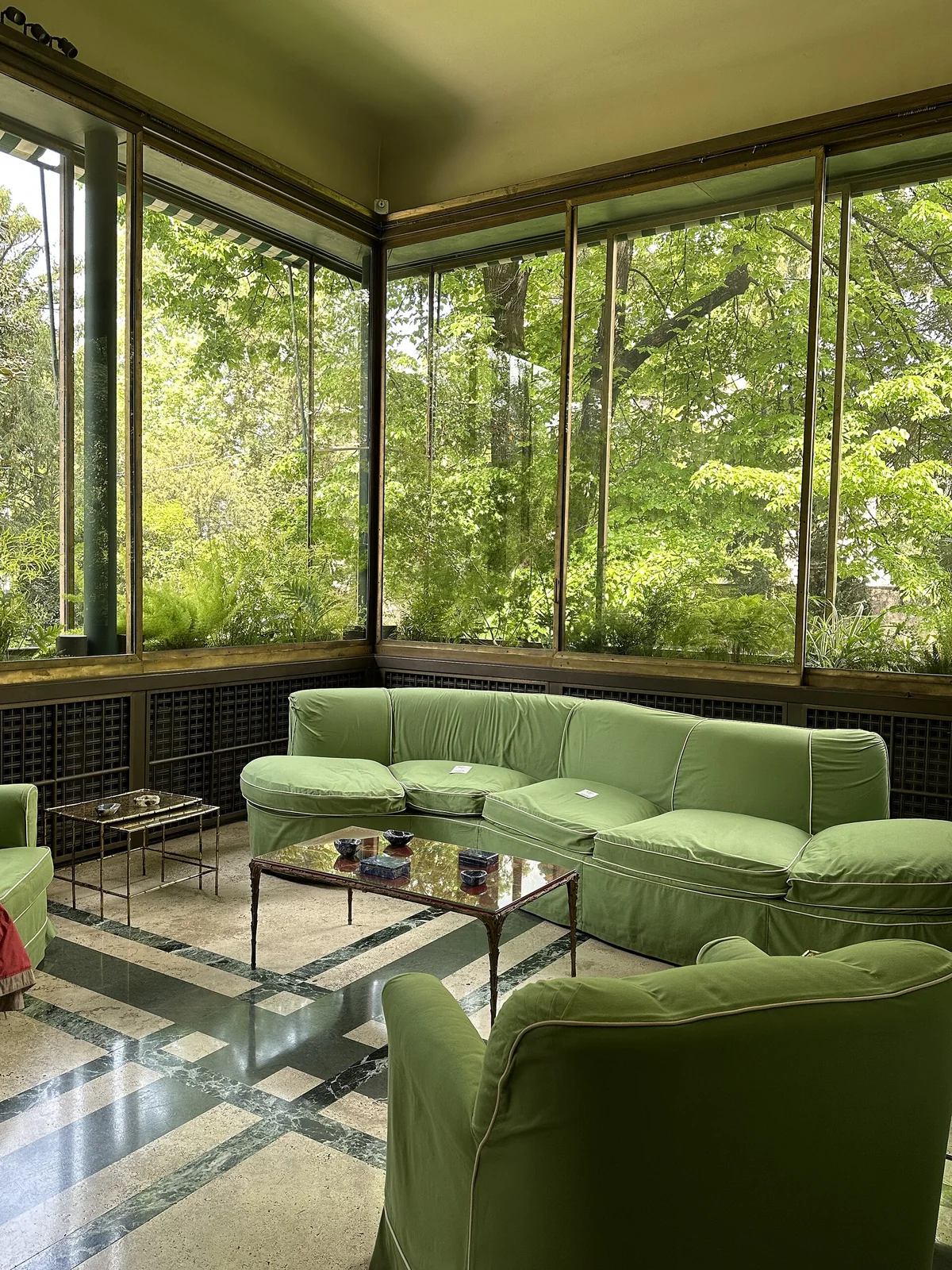 A glass walled veranda with green sofas, a green ceiling and trees outside the windows