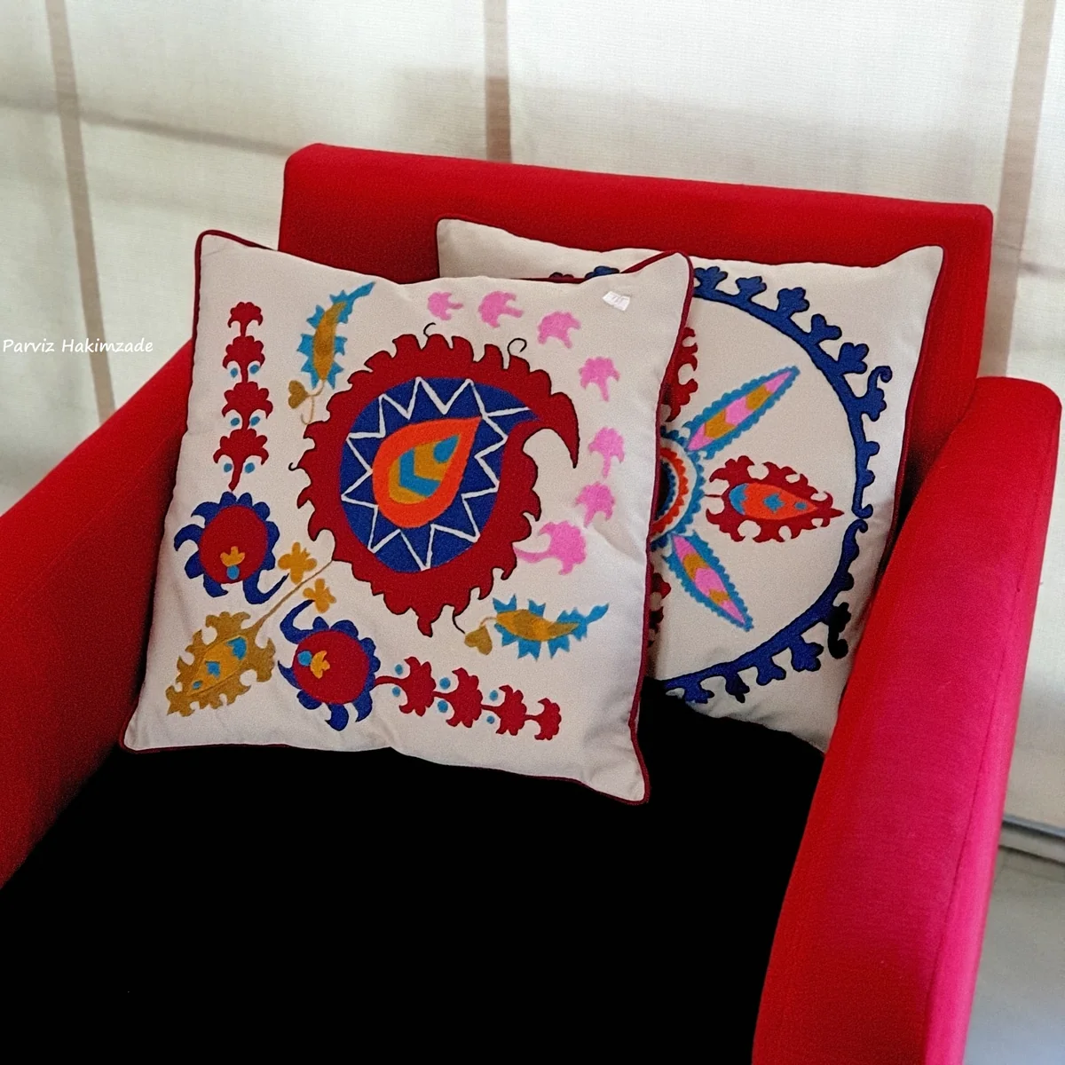 Two embroidered suzani cushions with red and blue floral medallions on a red armchair