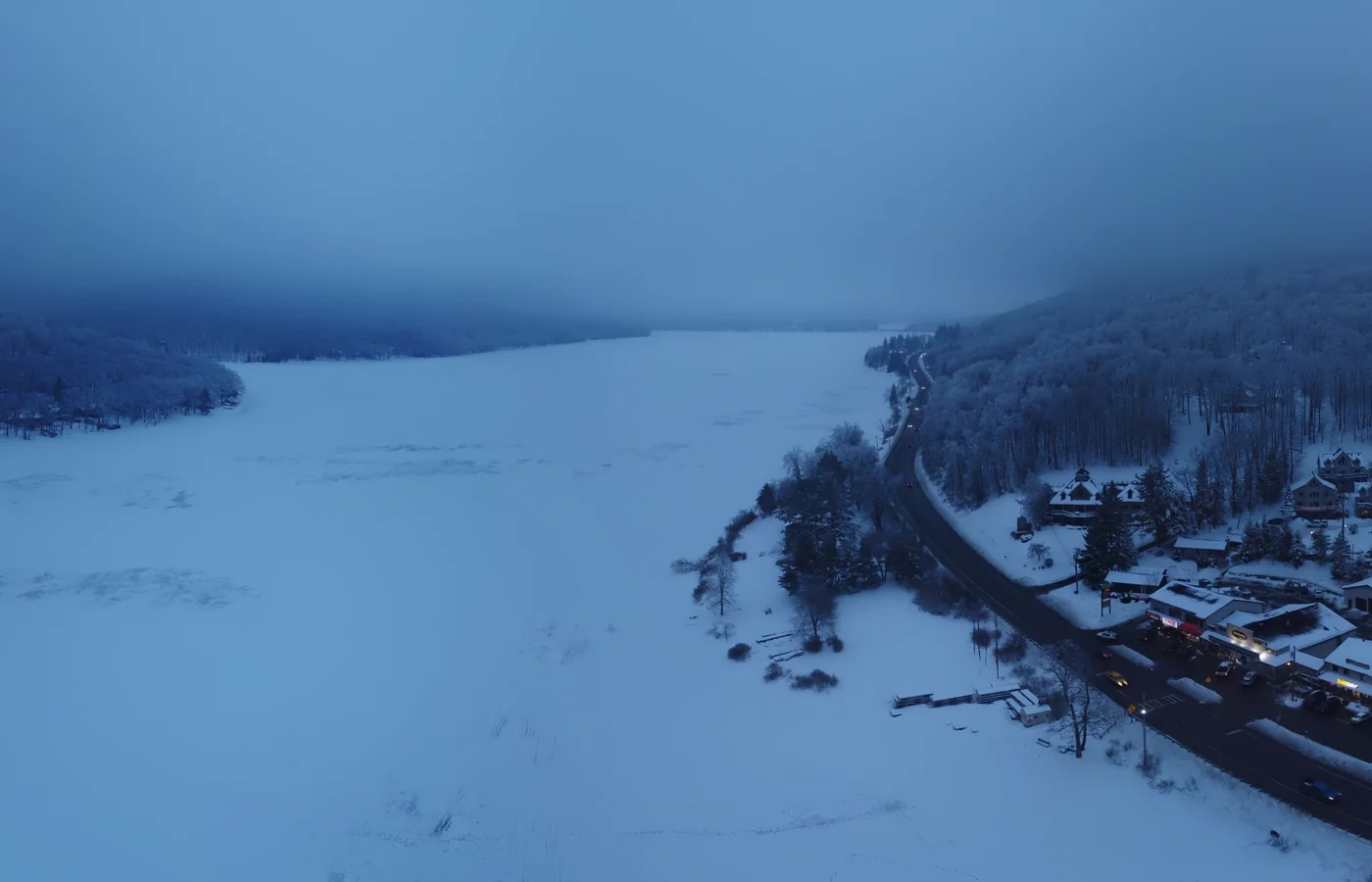Aerial view of a frozen, snow-covered Deep Creek Lake in winter, with houses along the shore road