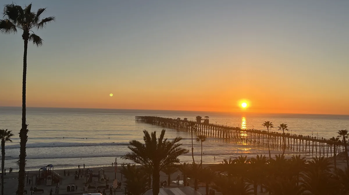 The sun setting beyond Oceanside Pier, with palms along the beach below, Oceanside, California