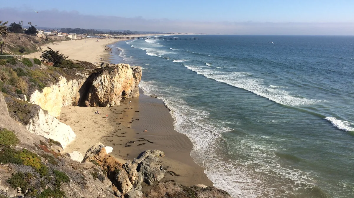 Sea cliffs and a sandy cove north of the Pismo Beach Pier, with the pier in the distance, California