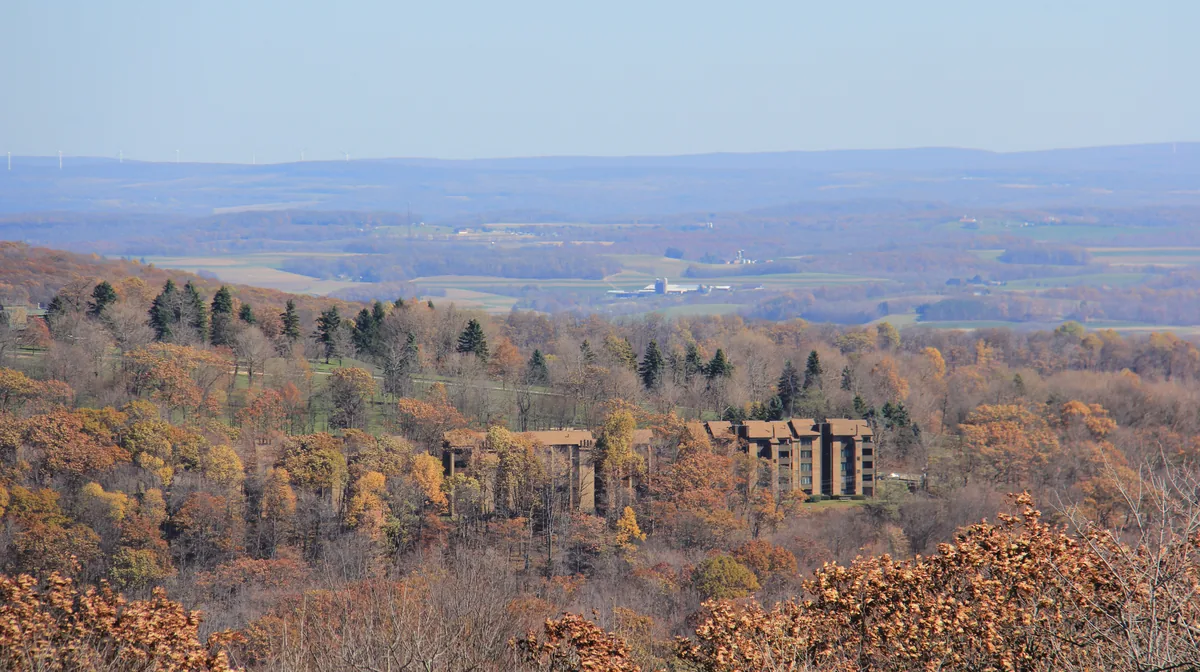 Buildings of Seven Springs Mountain Resort among the fall woods, with farmland beyond, Pennsylvania