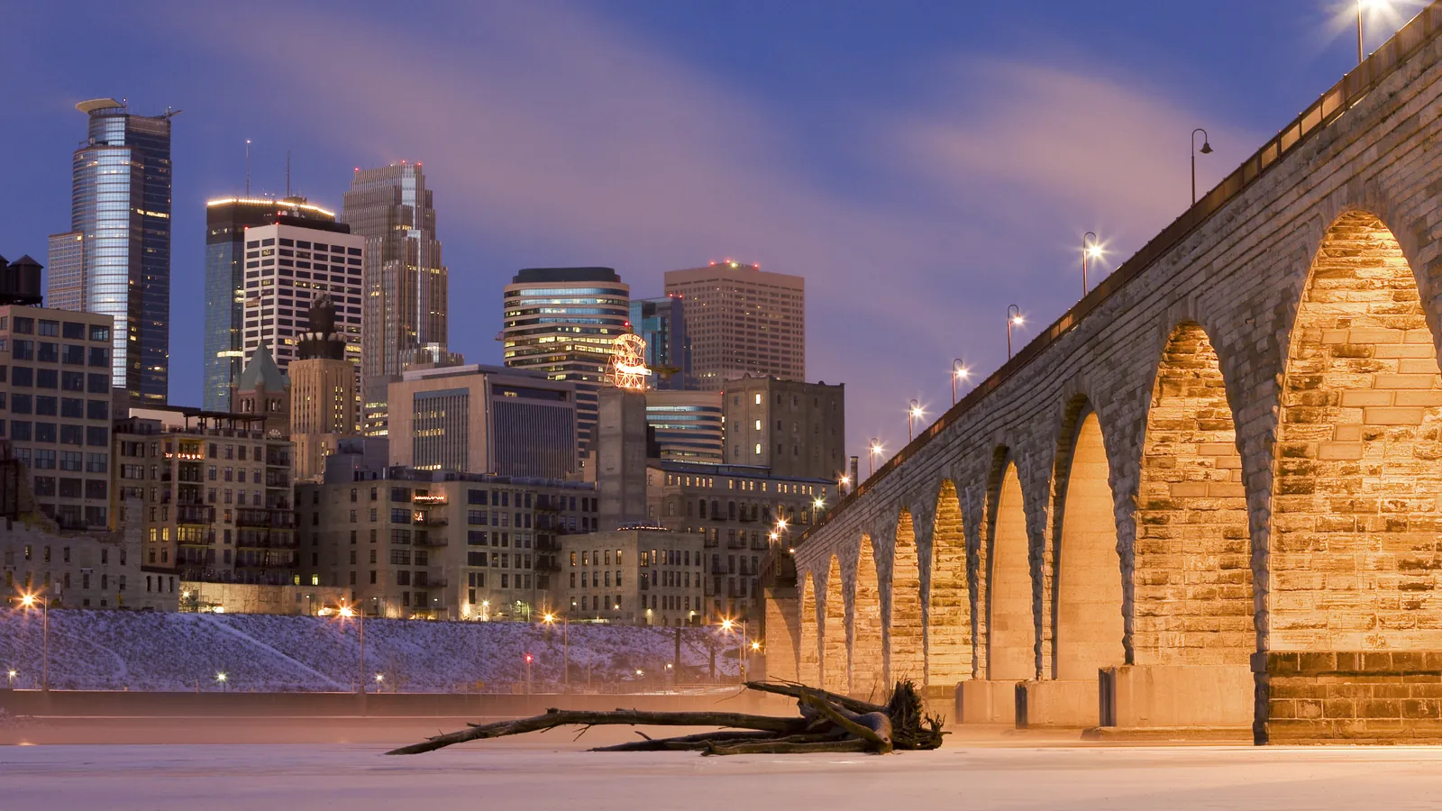 Stone Arch Bridge lit at dusk with the downtown Minneapolis skyline behind it